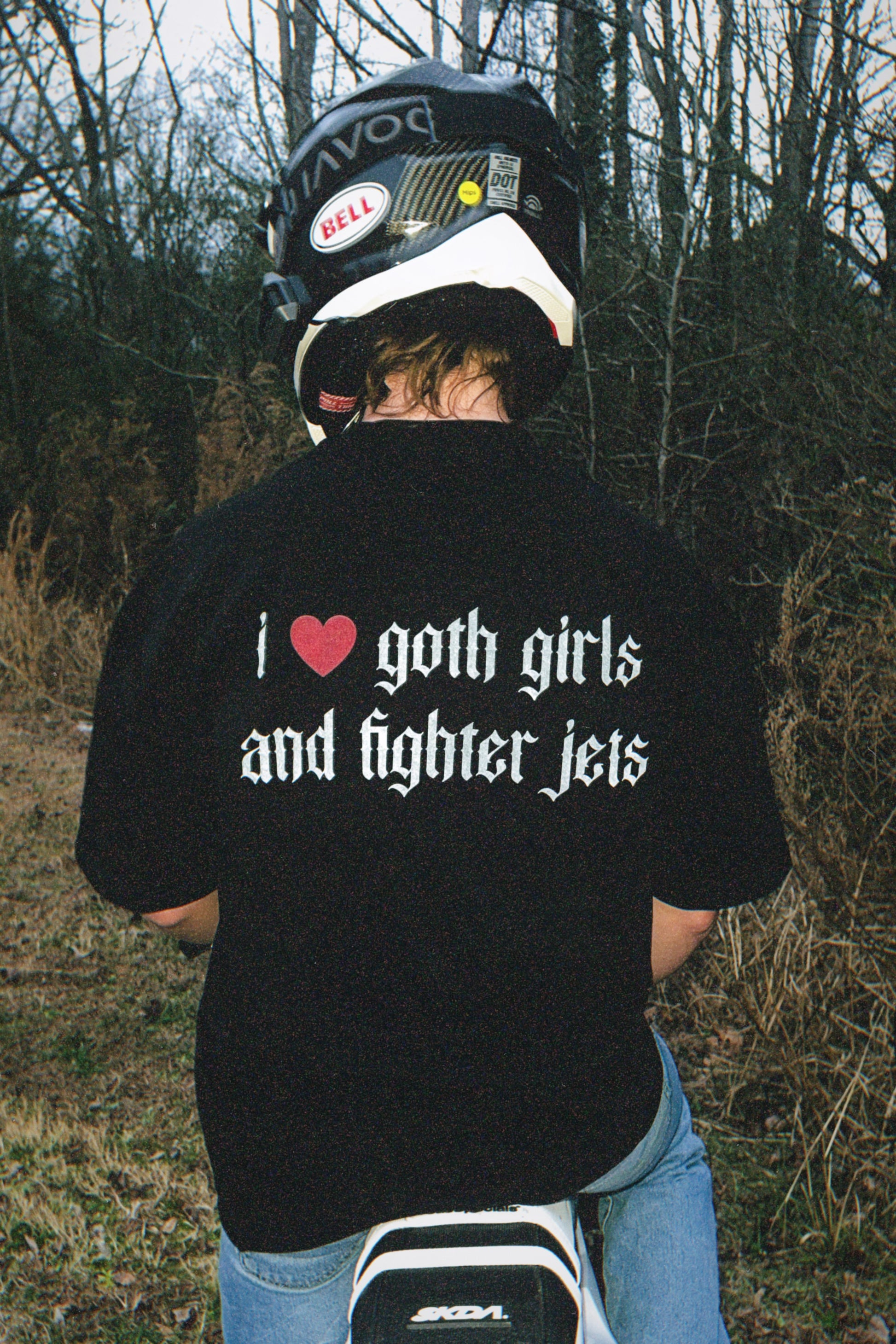 Person wearing helmet and black tee with 'I heart goth girls and fighter jets' text, outdoors
