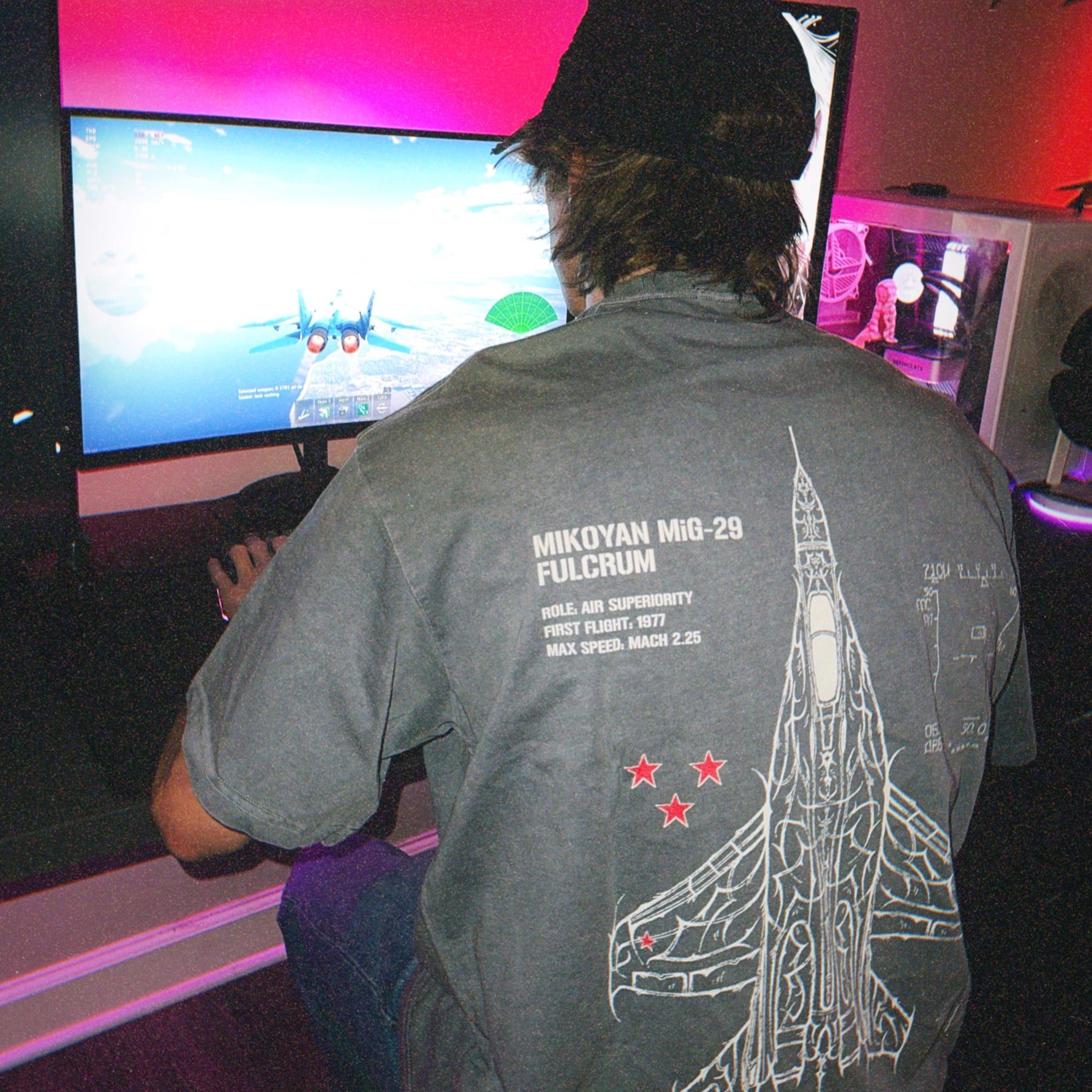 Person gaming in MiG-29 Fulcrum graphic tee at desktop, aviation streetwear, neon lighting