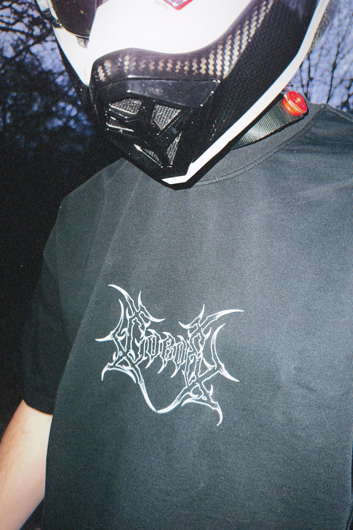 Close-up of person wearing a black graphic tee with white metal-style logo, motorcycle helmet