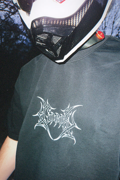 Close-up of person wearing a black graphic tee with white metal-style logo, motorcycle helmet