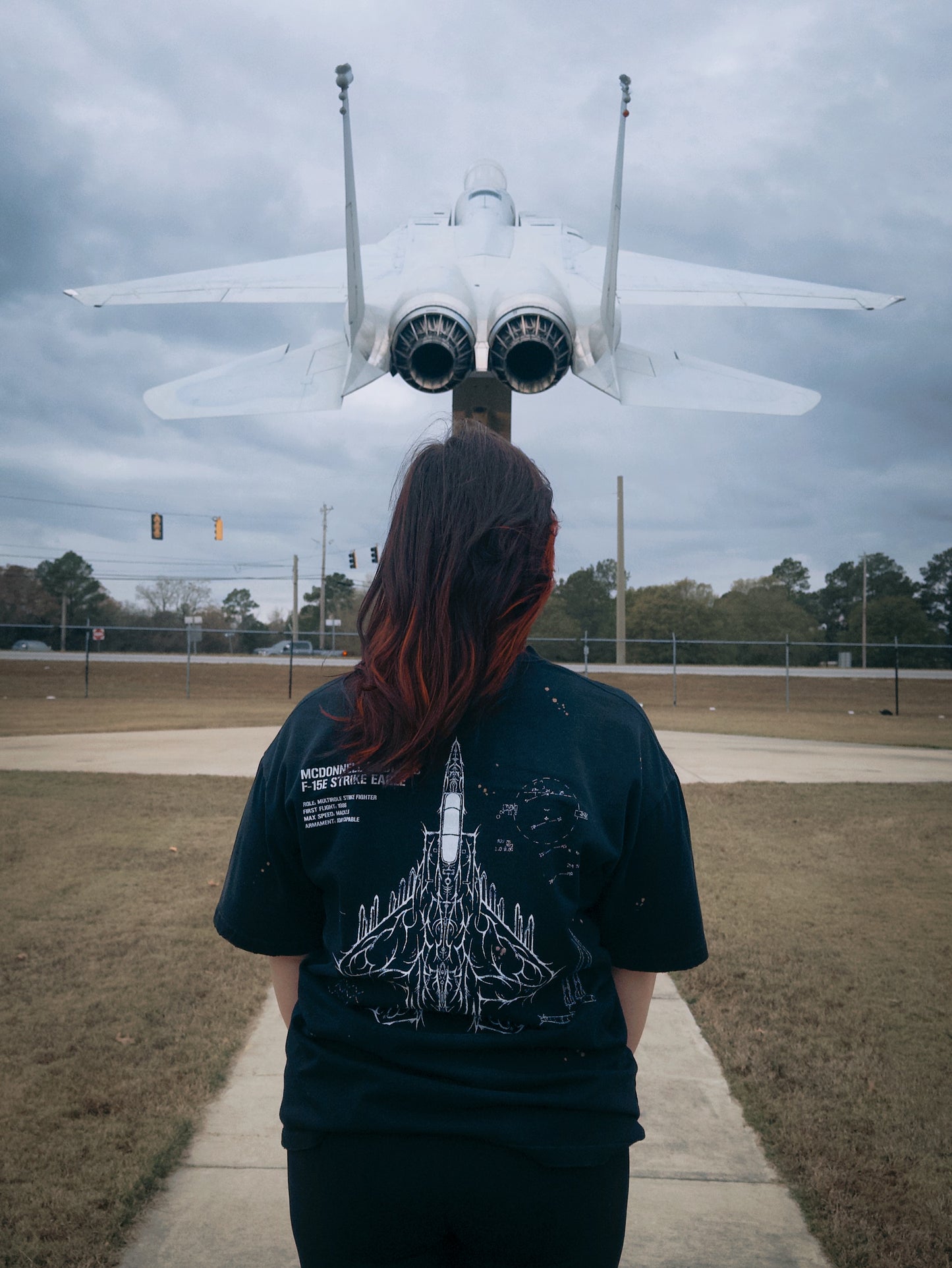Person wearing aviation-inspired graphic tee standing in front of fighter jet outdoors