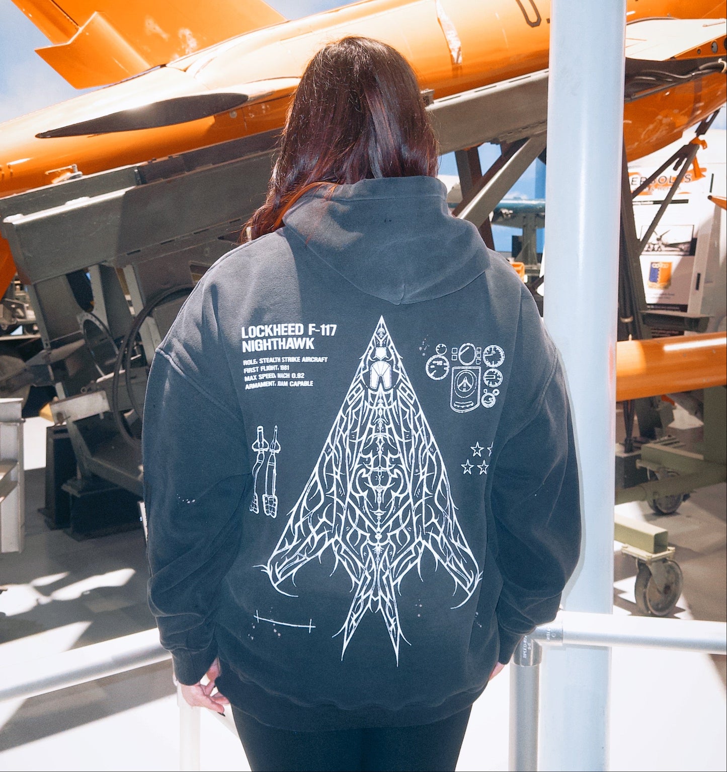 Person in black hoodie with Lockheed F-117 Nighthawk graphic, standing near aircraft exhibit