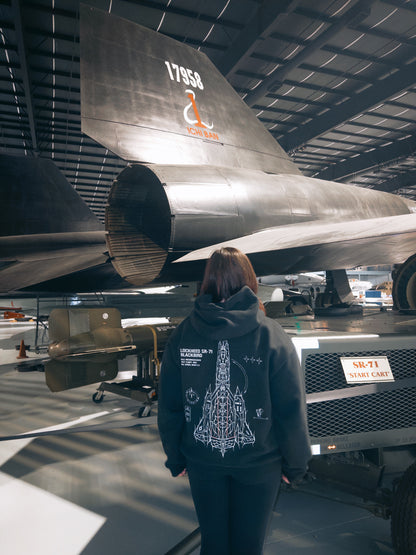 Person wearing aviation streetwear hoodie with SR-71 Blackbird graphic, standing by aircraft