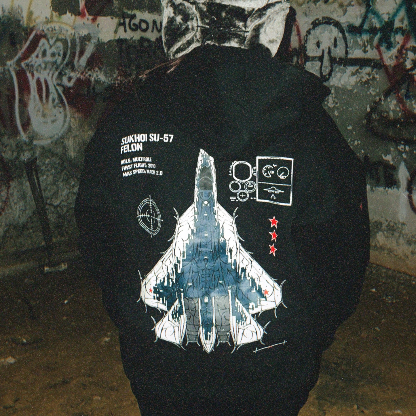 Person wearing black streetwear hoodie with aviation-inspired Sukhoi SU-57 jet graphic design