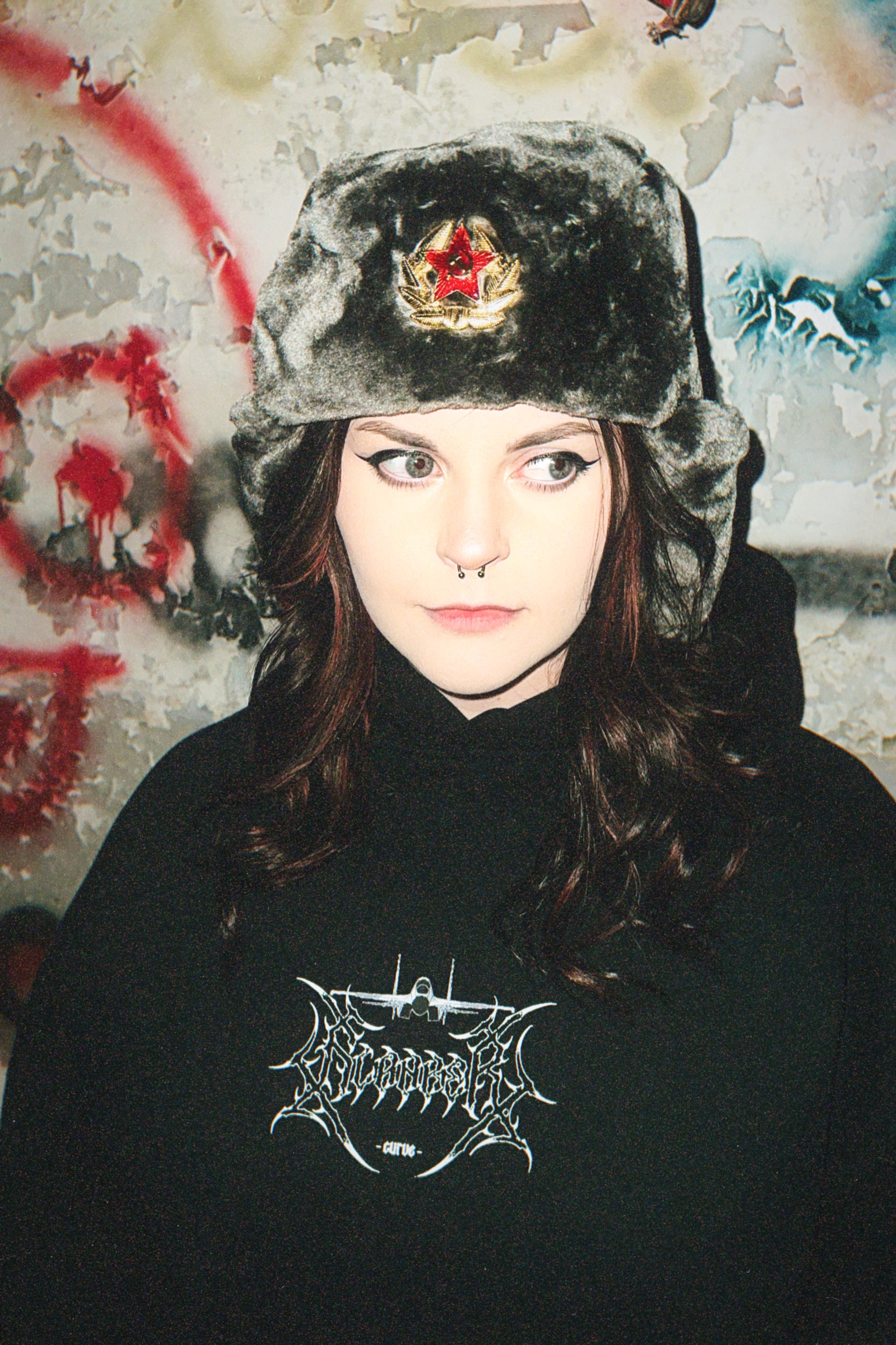 Woman in a fur hat with red star badge and black graphic hoodie, grunge urban background