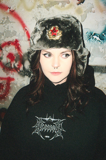Woman in a fur hat with red star badge and black graphic hoodie, grunge urban background