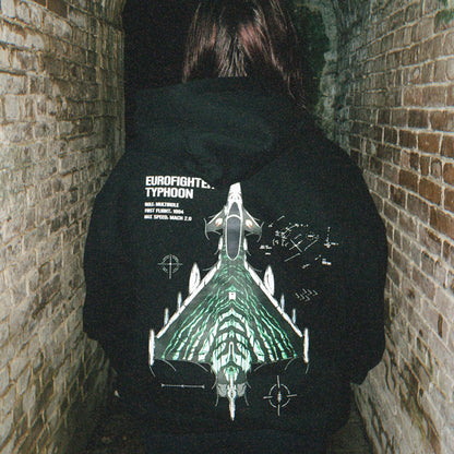 Person in alley wears black hoodie with Eurofighter Typhoon jet graphic, aviation streetwear