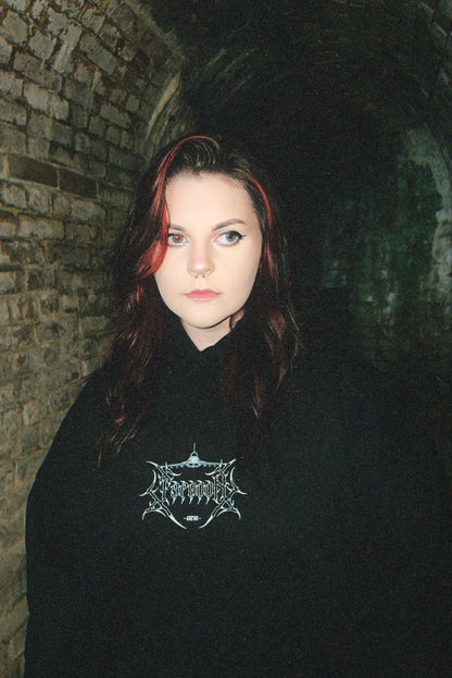 Woman in black graphic streetwear hoodie with linework design, standing in dim brick tunnel