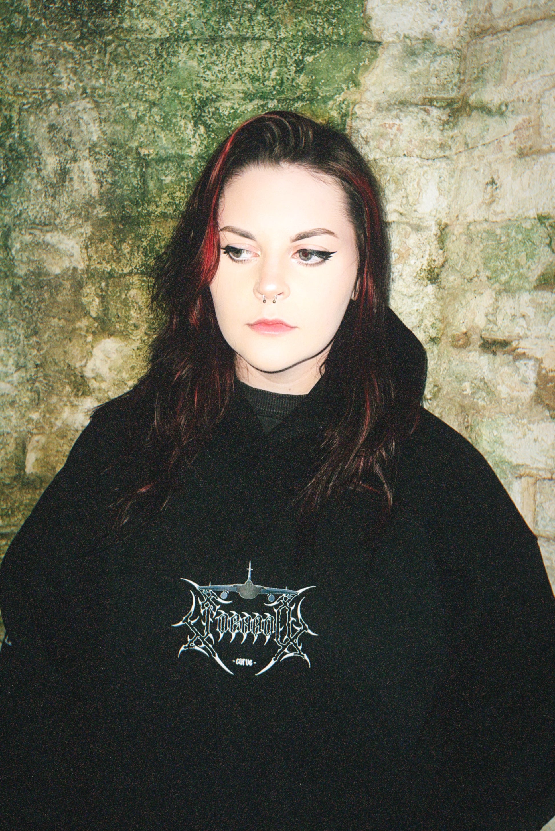 Woman in black aviation-inspired graphic hoodie with linework design, standing by textured stone wall