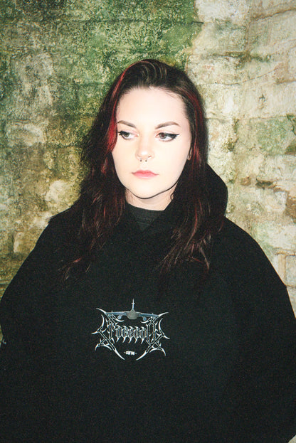 Woman in black aviation-inspired graphic hoodie with linework design, standing by textured stone wall