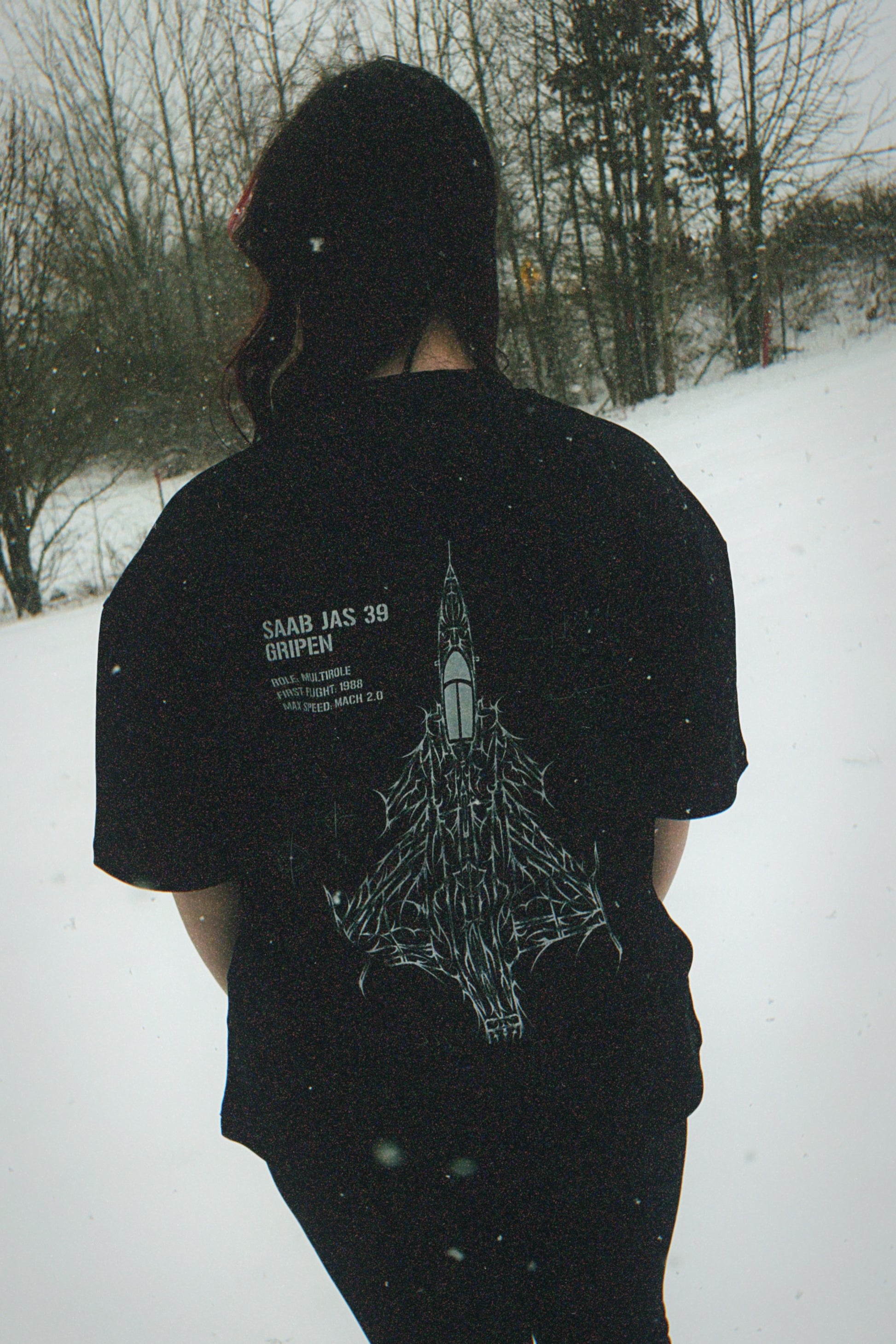 Person wearing black t-shirt with Saab JAS 39 Gripen fighter jet graphic in snowy outdoor setting