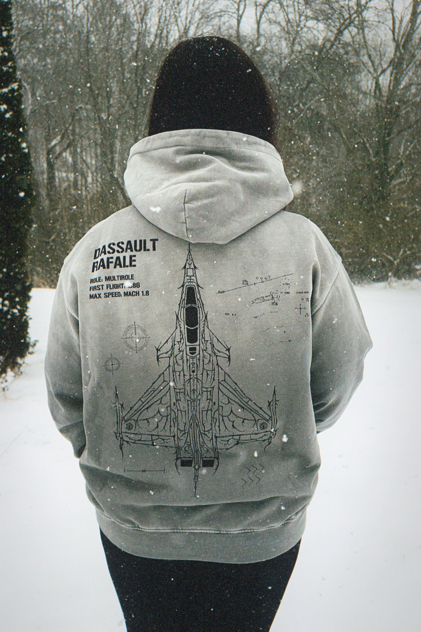 Person wearing a grey hoodie with Dassault Rafale jet graphic and specs, outdoors in snow