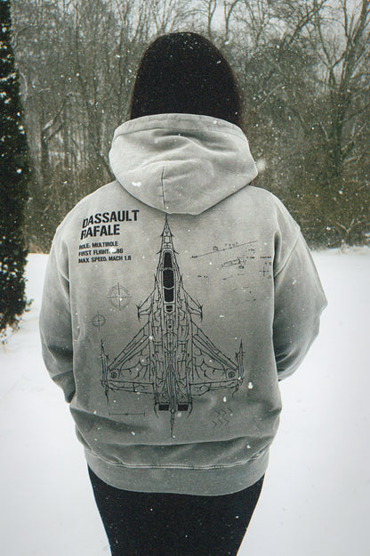 Person wearing a grey hoodie with Dassault Rafale jet graphic and specs, outdoors in snow