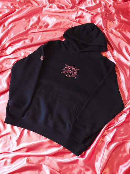 Black hoodie with pink graphic linework on chest, displayed on pink satin fabric