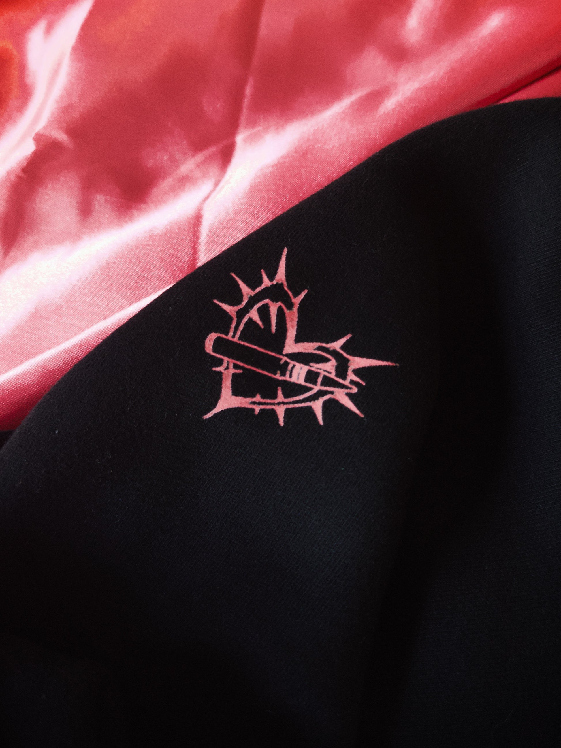 Black streetwear fabric with pink aviation-inspired heart and missile graphic, pink satin background