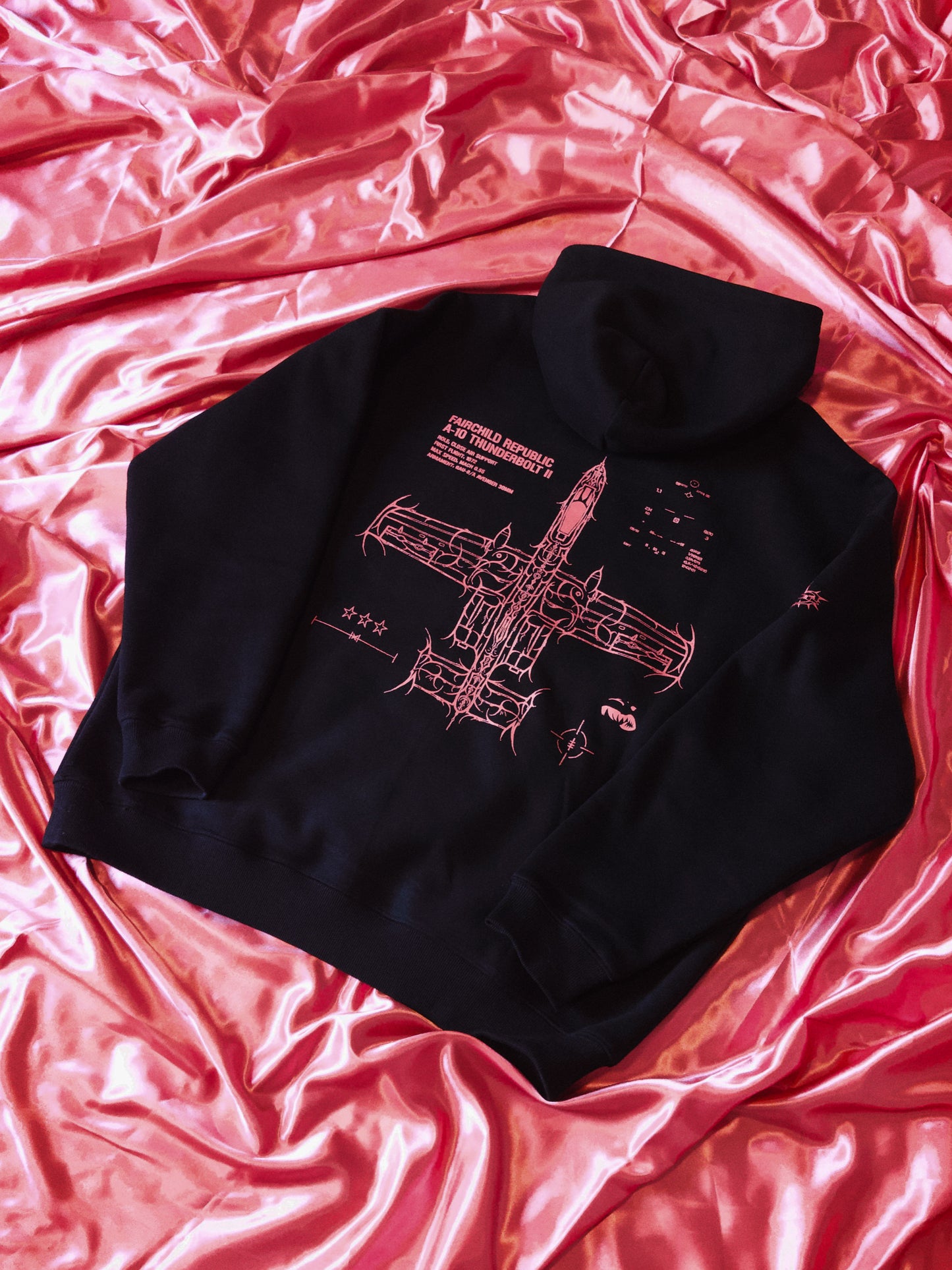 Black hoodie with pink aviation blueprint graphic, displayed on pink satin fabric