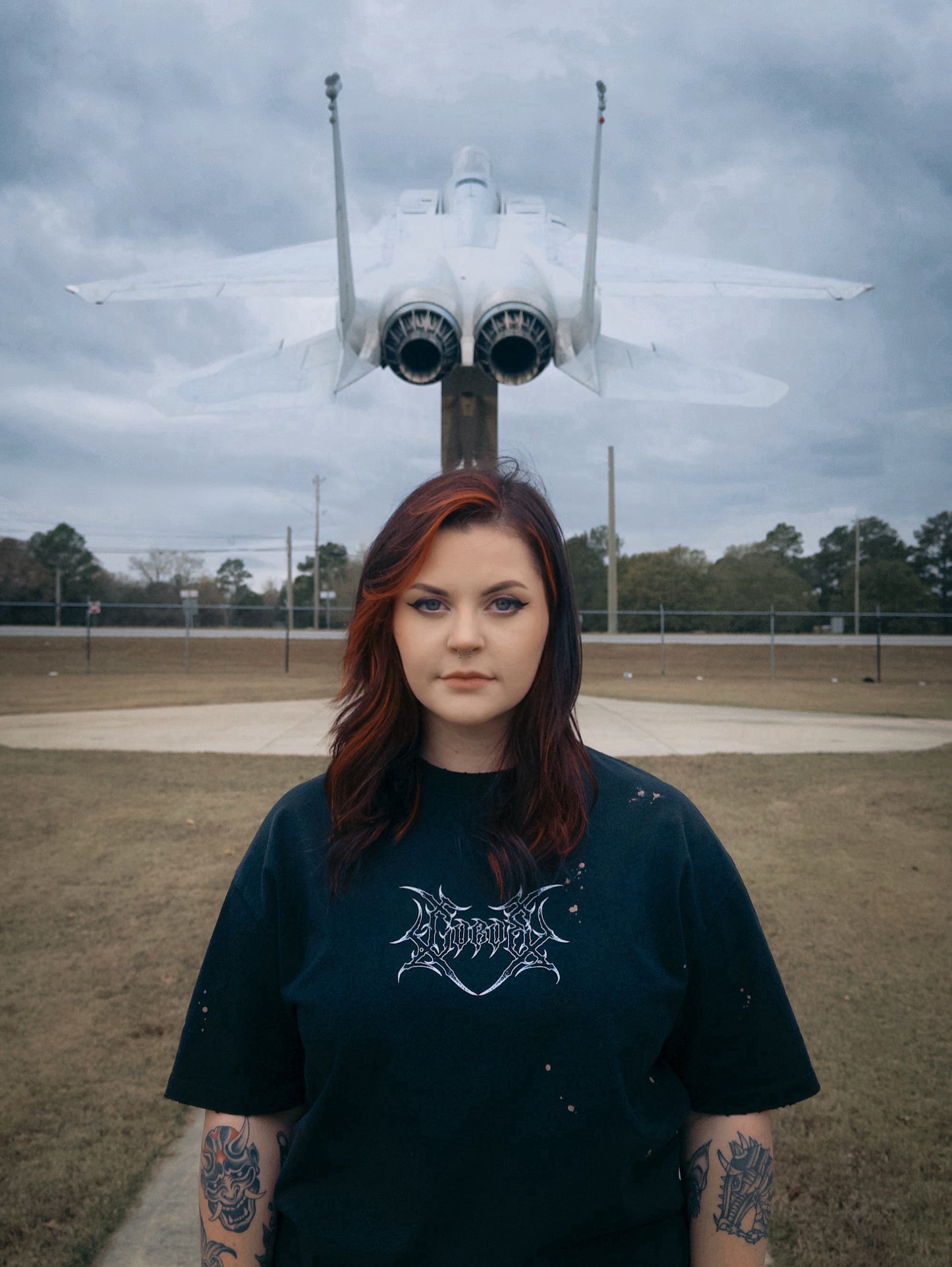 Woman in distressed tee with tattoos standing in front of military jet outdoors