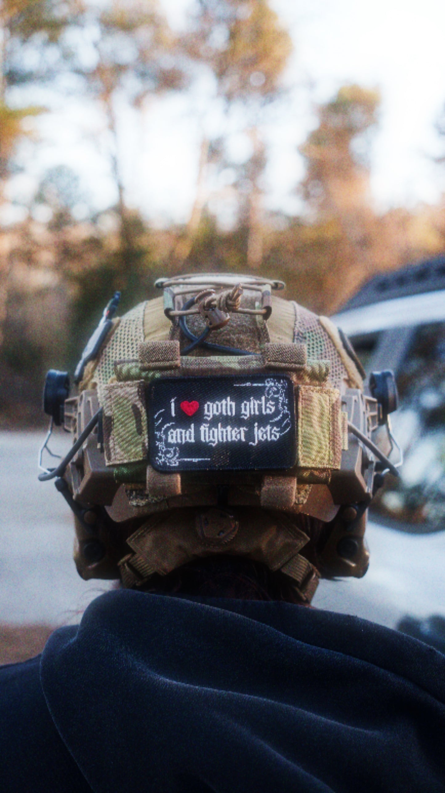 Tactical helmet with patch reading 'I love goth girls and fighter jets', outdoor setting