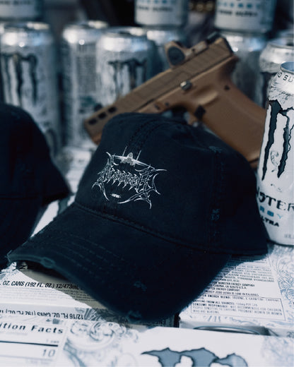 Black distressed cap with aviation-inspired logo, surrounded by energy drink cans and a tan prop item