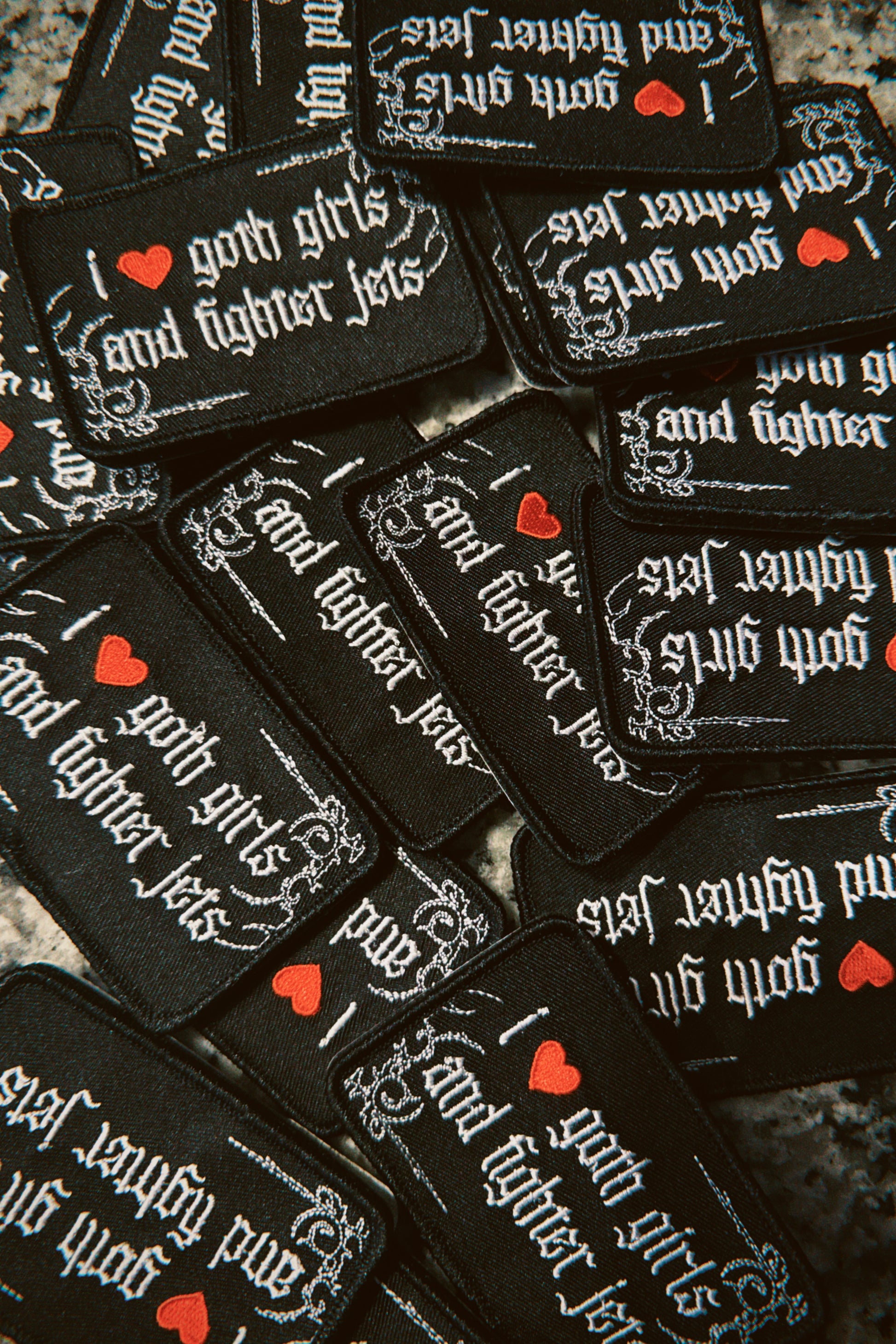 Pile of black embroidered patches with gothic text reading 'I love goth girls and fighter jets'.
